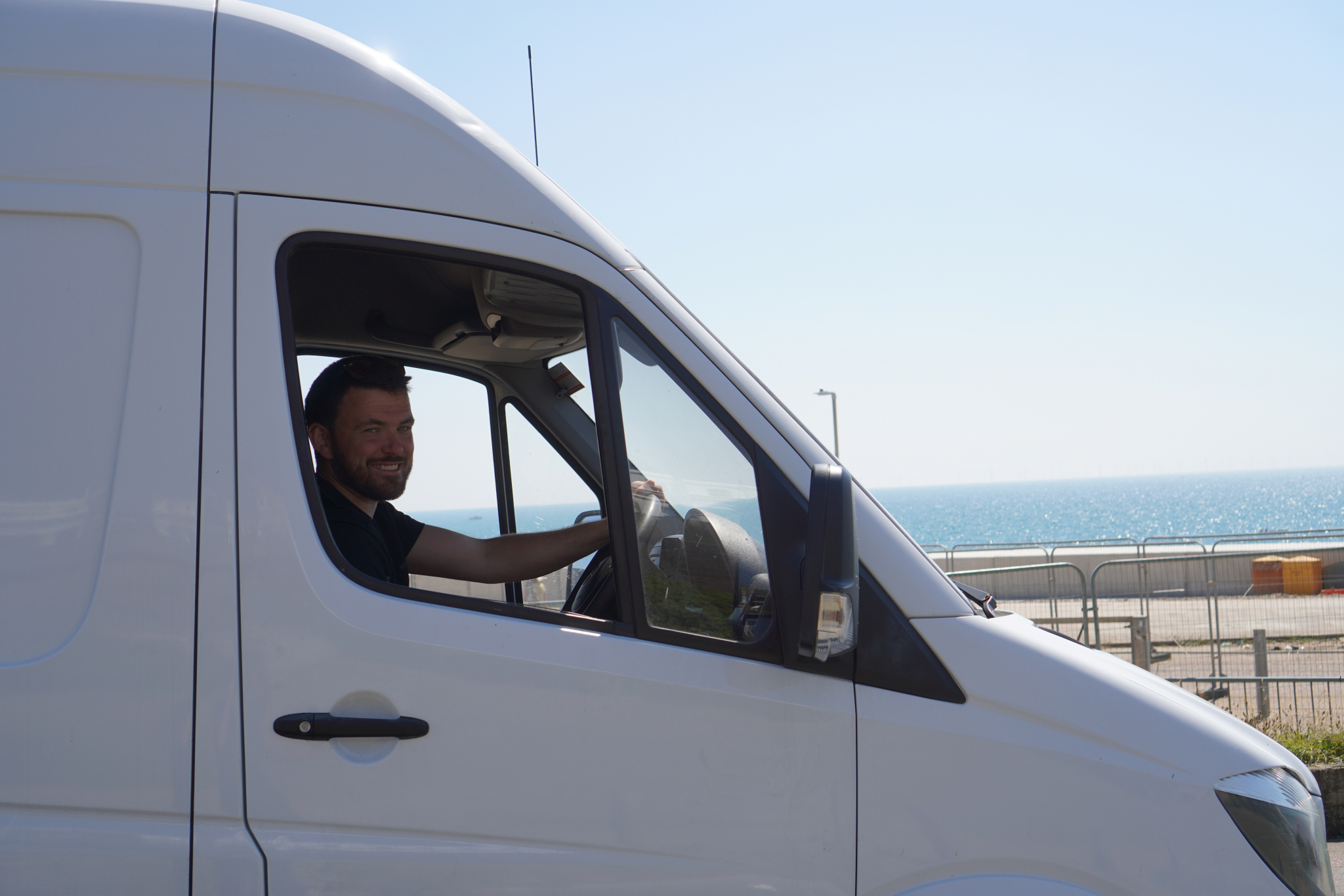 Peter Hawes smiling from the driver’s seat of the ESV Removals Mercedes Sprinter, parked above the sea on the coast east of Brighton
