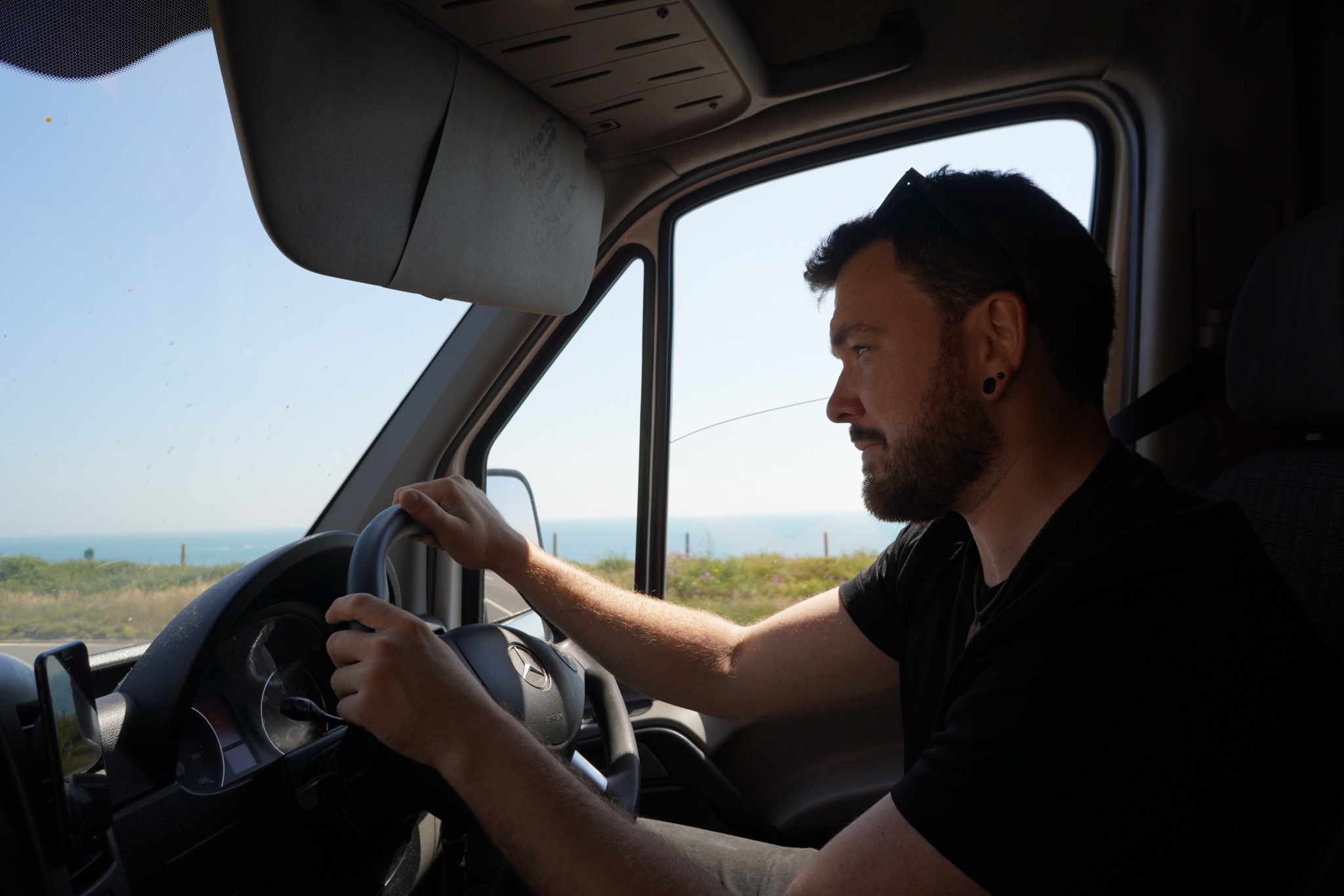 Peter Hawes driving the ESV Removals Sprinter along the coast, with the sea and the horizon through the side window
