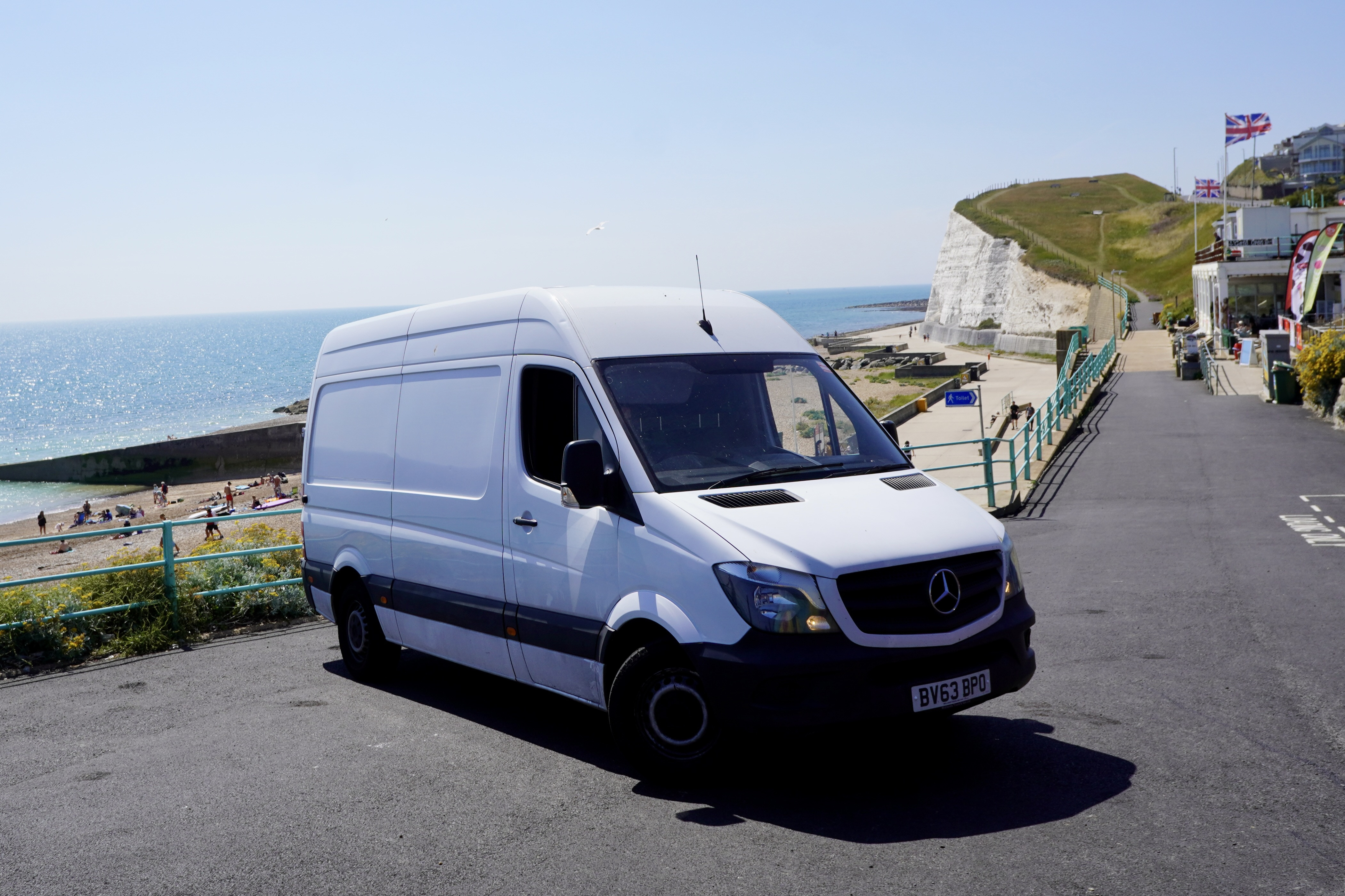 ESV Removals Mercedes Sprinter parked on an exposed cliff-top road east of Brighton, with a white chalk cliff and the sea behind