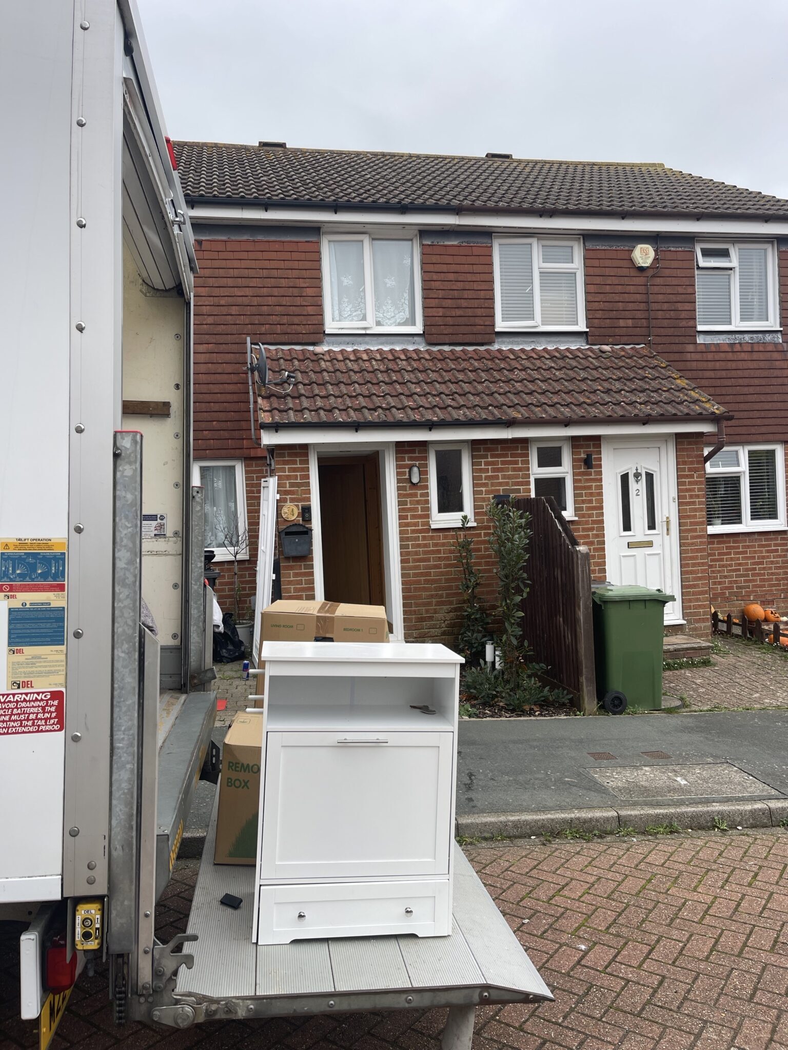 White cabinet and removal boxes on the tail lift of a Luton van outside a terraced house during a Brighton removals job.