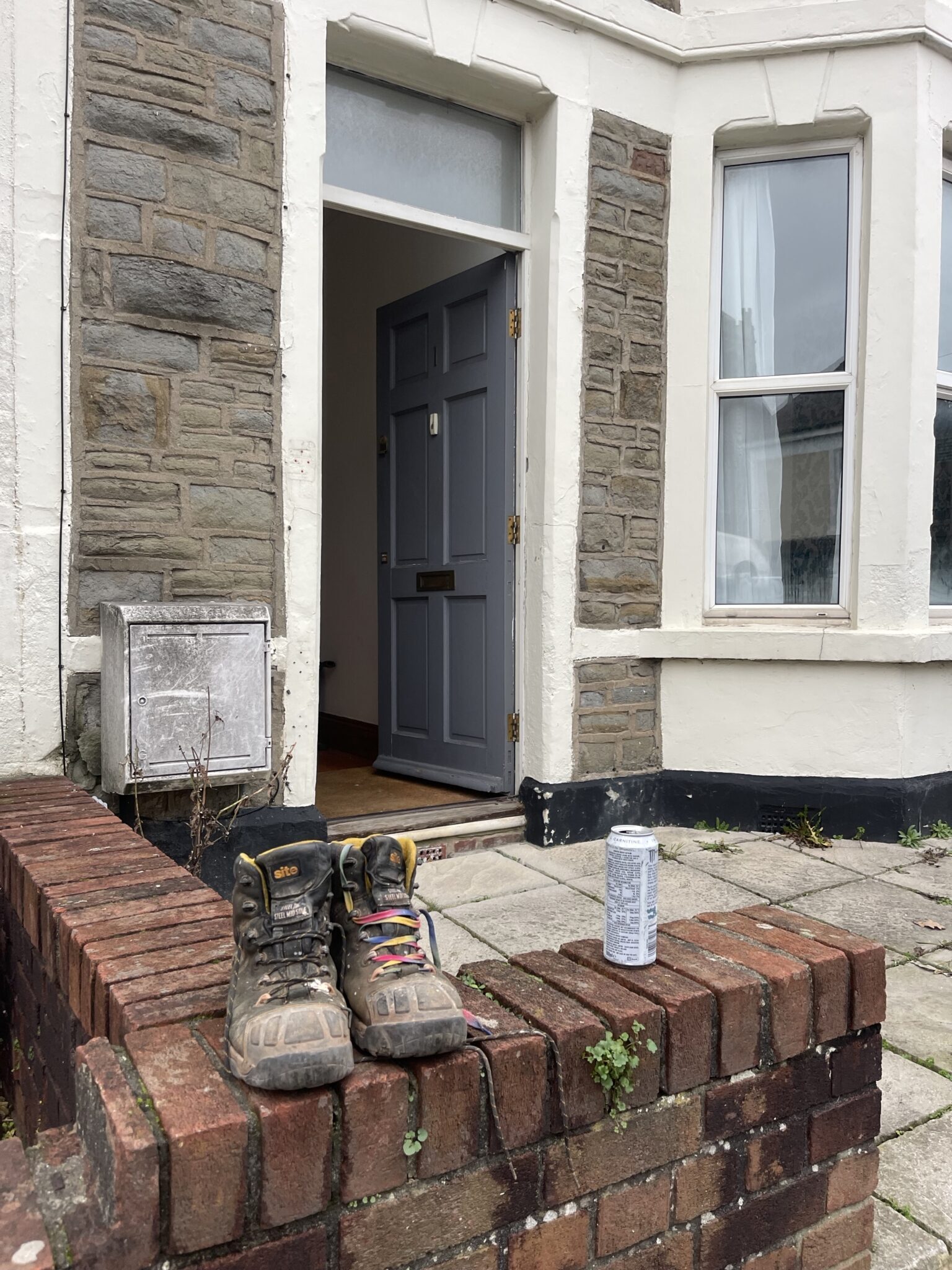 Work boots on a brick wall outside a Brighton terrace with the front door open, showing a new home being prepped before moving in.