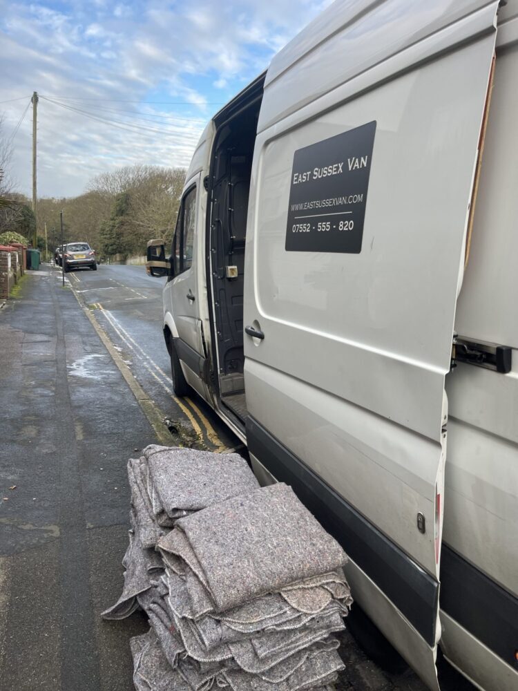 ESV Removals Mercedes Sprinter man and van parked on a Sussex residential road with moving blankets stacked on the pavement ready for a Brighton move.