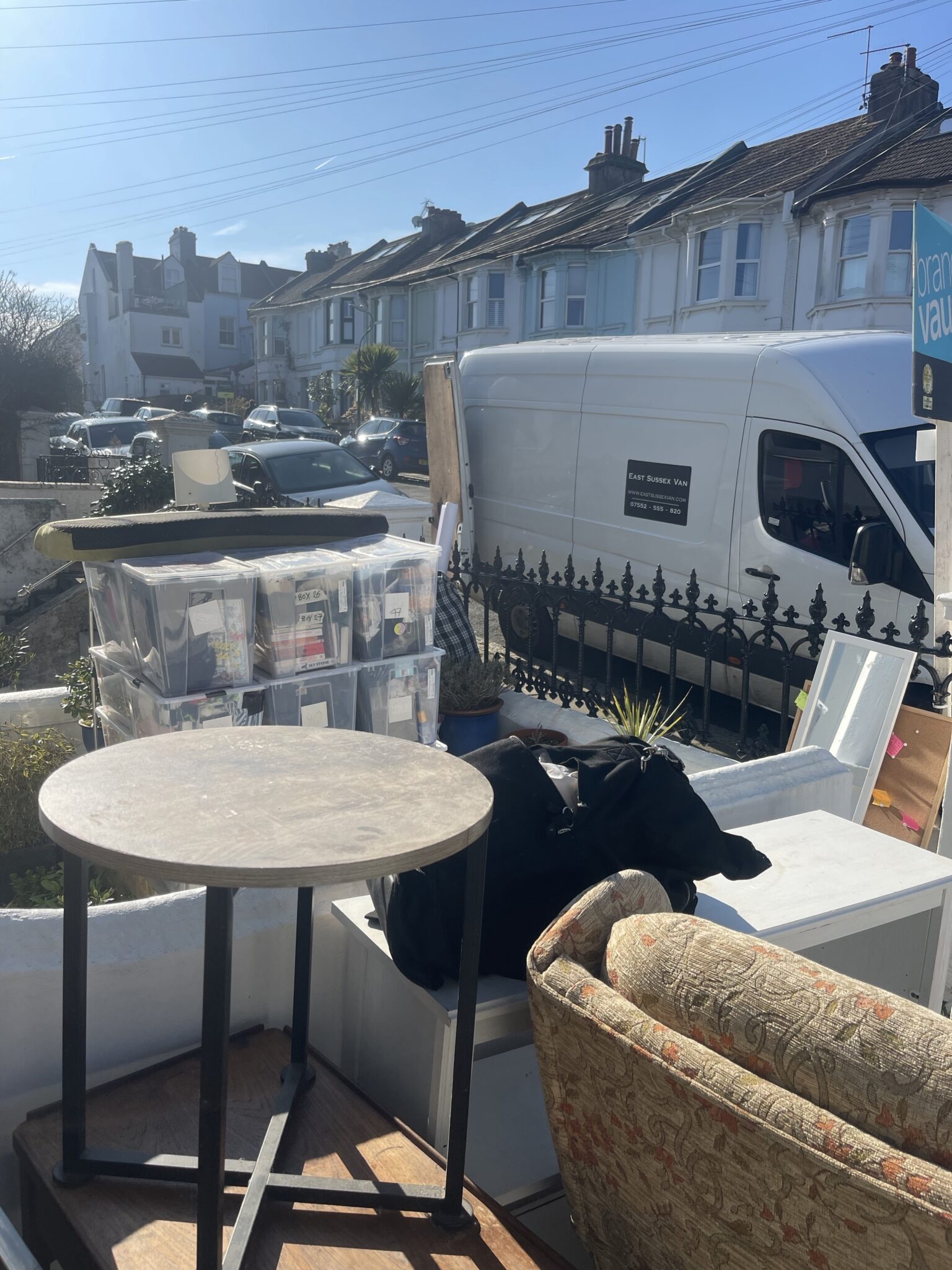 Household items and labelled storage boxes staged outside a Brighton home in Preston Park, with an ESV removals van parked on the street in the background.
