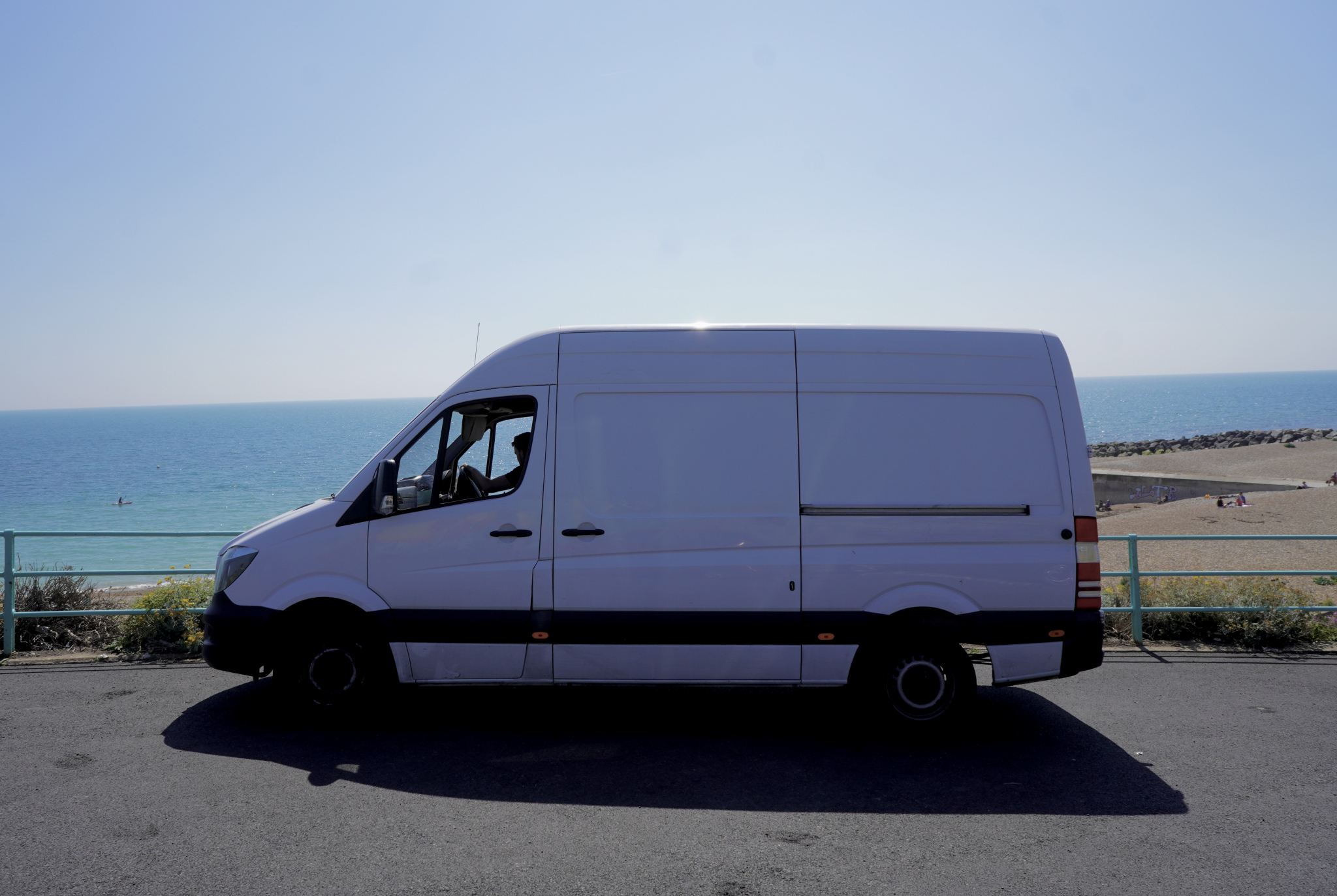 Side view of a white Mercedes Sprinter removals van parked by the sea on the Brighton and Hove seafront on a sunny day.