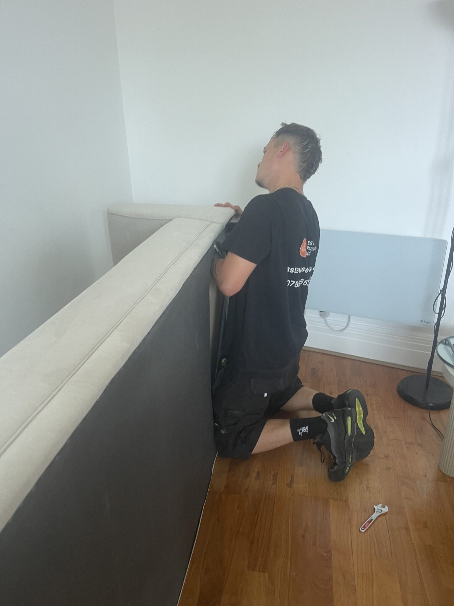 ESV Removals crew member kneeling to dismantle a large upholstered bed headboard in a bedroom before the carry