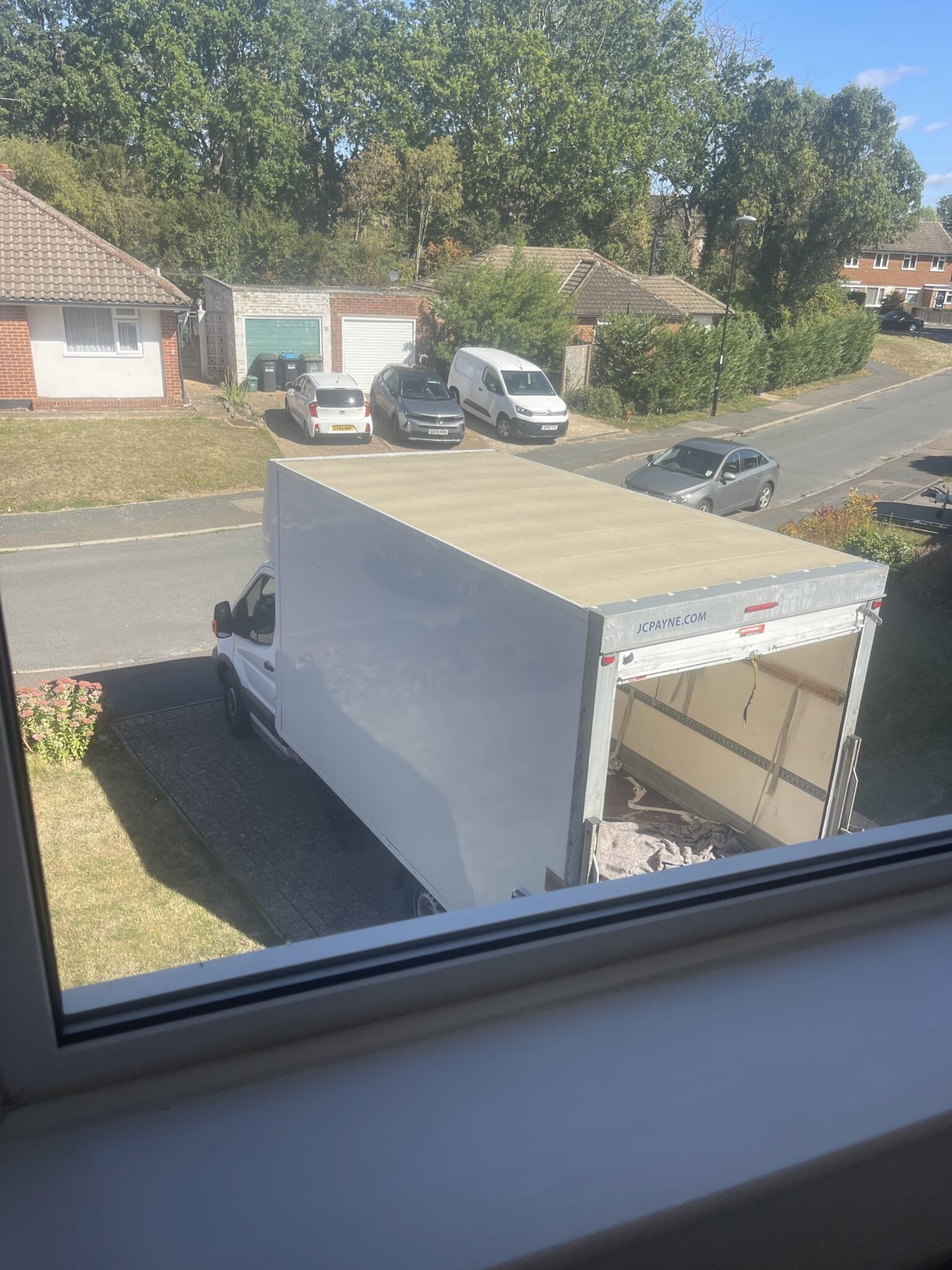 ESV Removals Luton van with its rear open, backed onto a front lawn on a Burgess Hill residential road, seen from an upstairs window