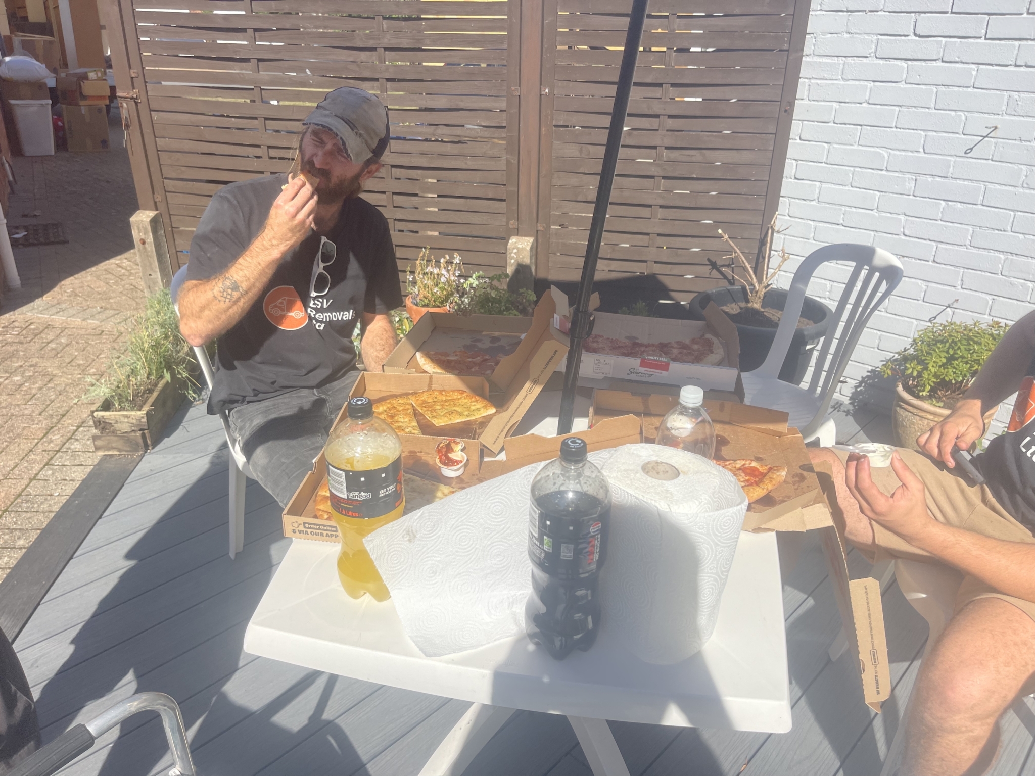 ESV Removals crew member in a branded t-shirt eating pizza at an outdoor table during a lunch break on a Burgess Hill house move