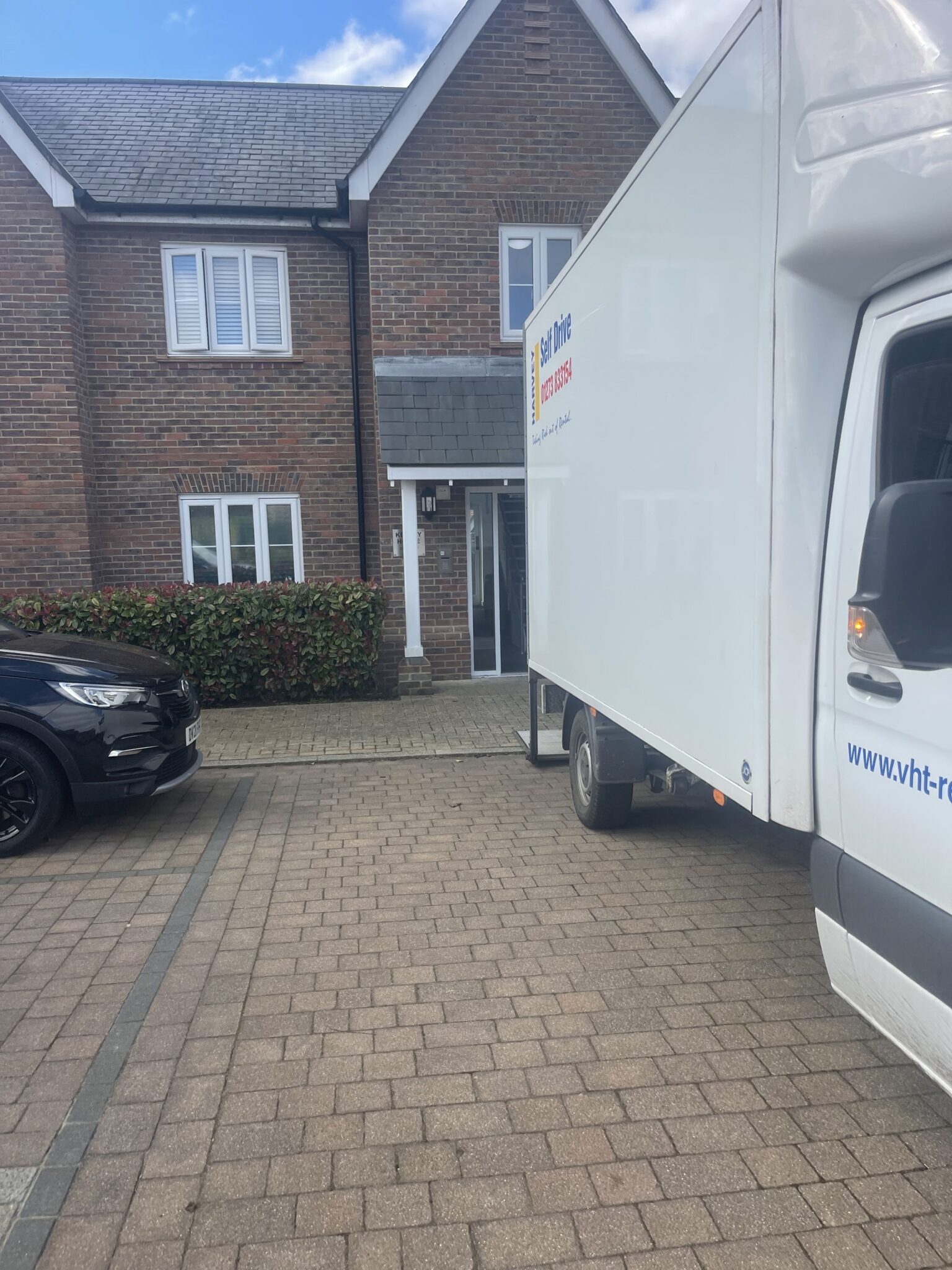 Luton removals van parked outside a modern brick townhouse in Burgess Hill during a residential move, showing easy driveway access and close loading position.