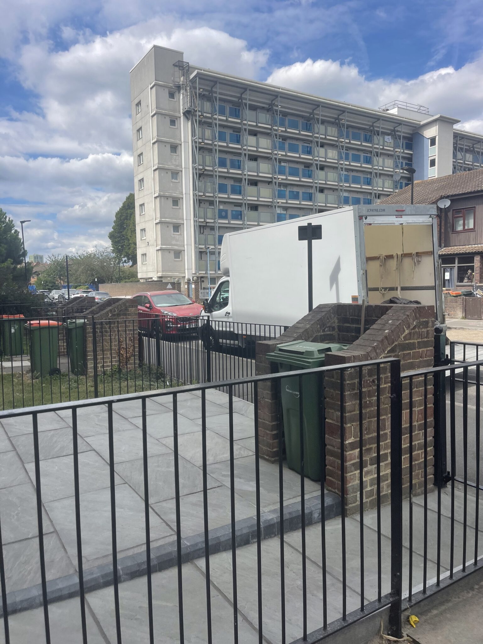 White ESV Luton removals van parked on-street beside a residential building in Canning Town, E16, with a tall Newham tower block behind and Newham London green wheelie bins in the foreground during a one room move collection.