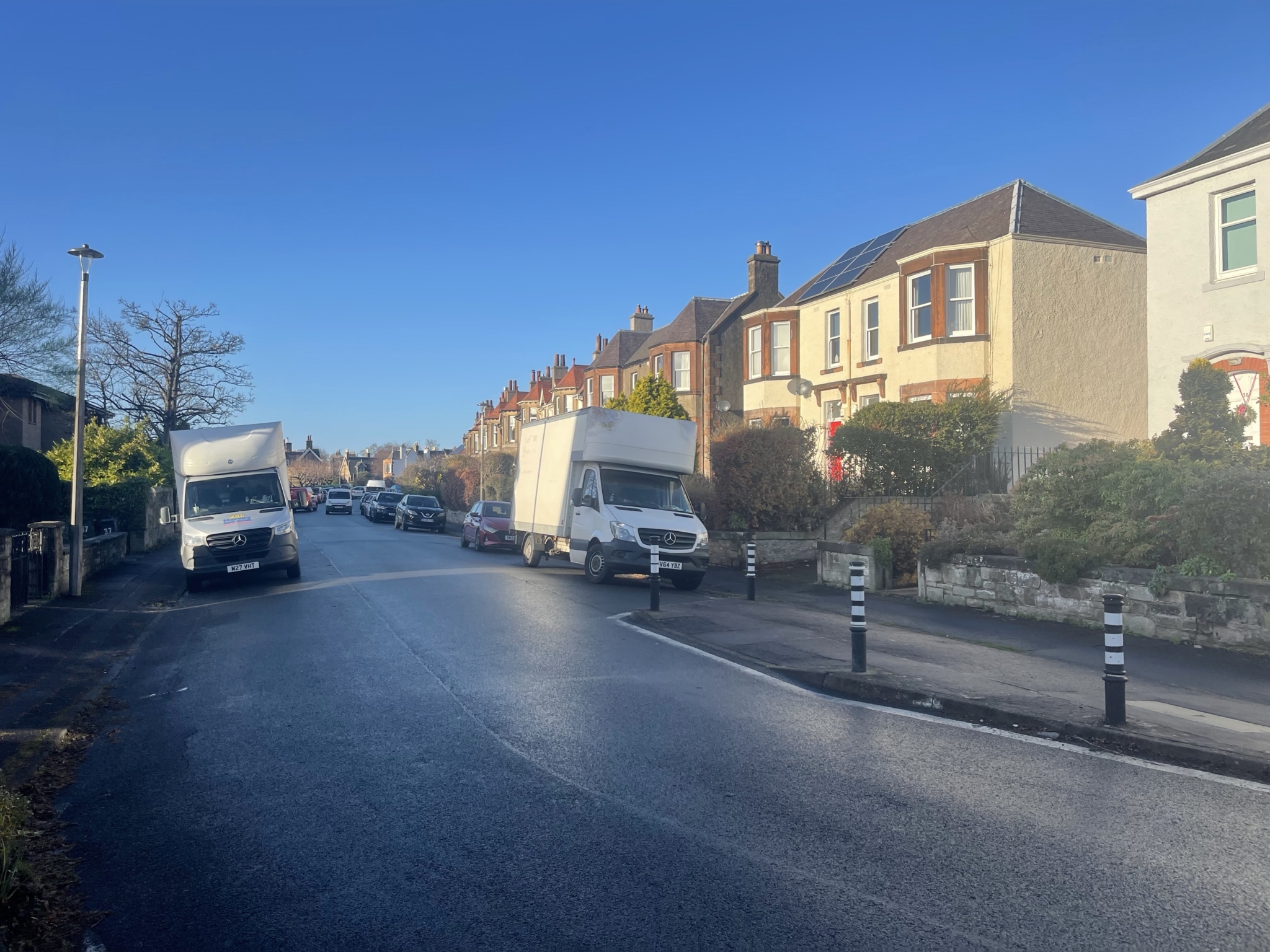 Two Luton removal vans parked on a quiet Edinburgh residential street lined with sandstone and rendered villas, black and white bollards along the kerb
