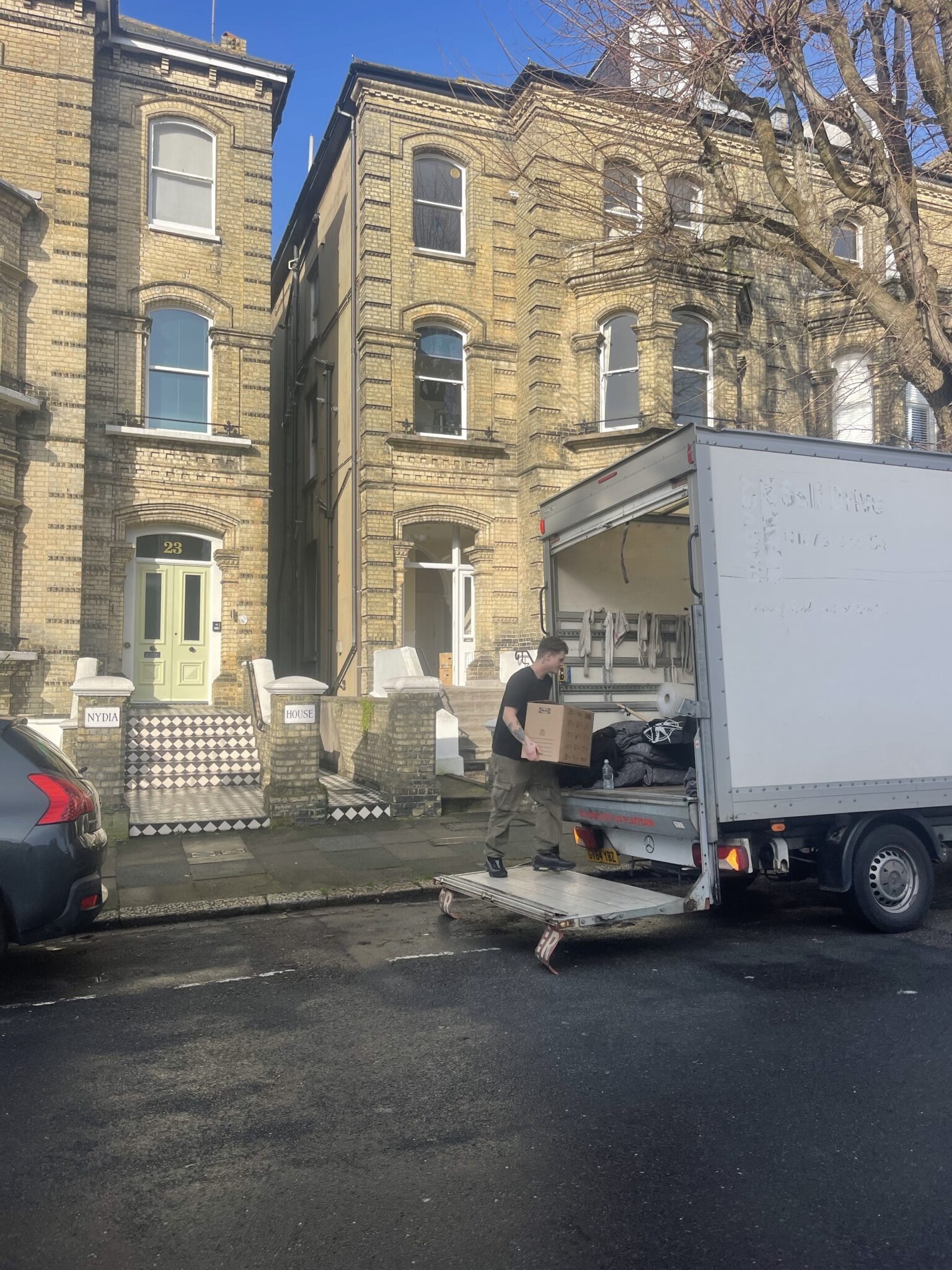 Removals van with tail lift down outside a central Hove period property, with a mover carrying a cardboard box into the van on a clear day.