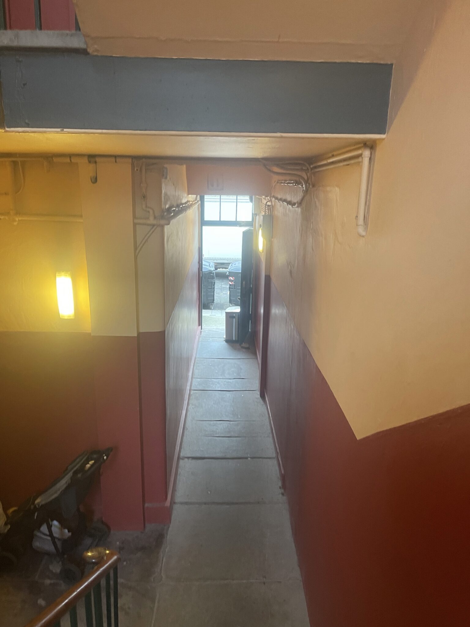 A long communal entrance passage with painted walls and a stone floor, leading through to the stairs of a block of flats