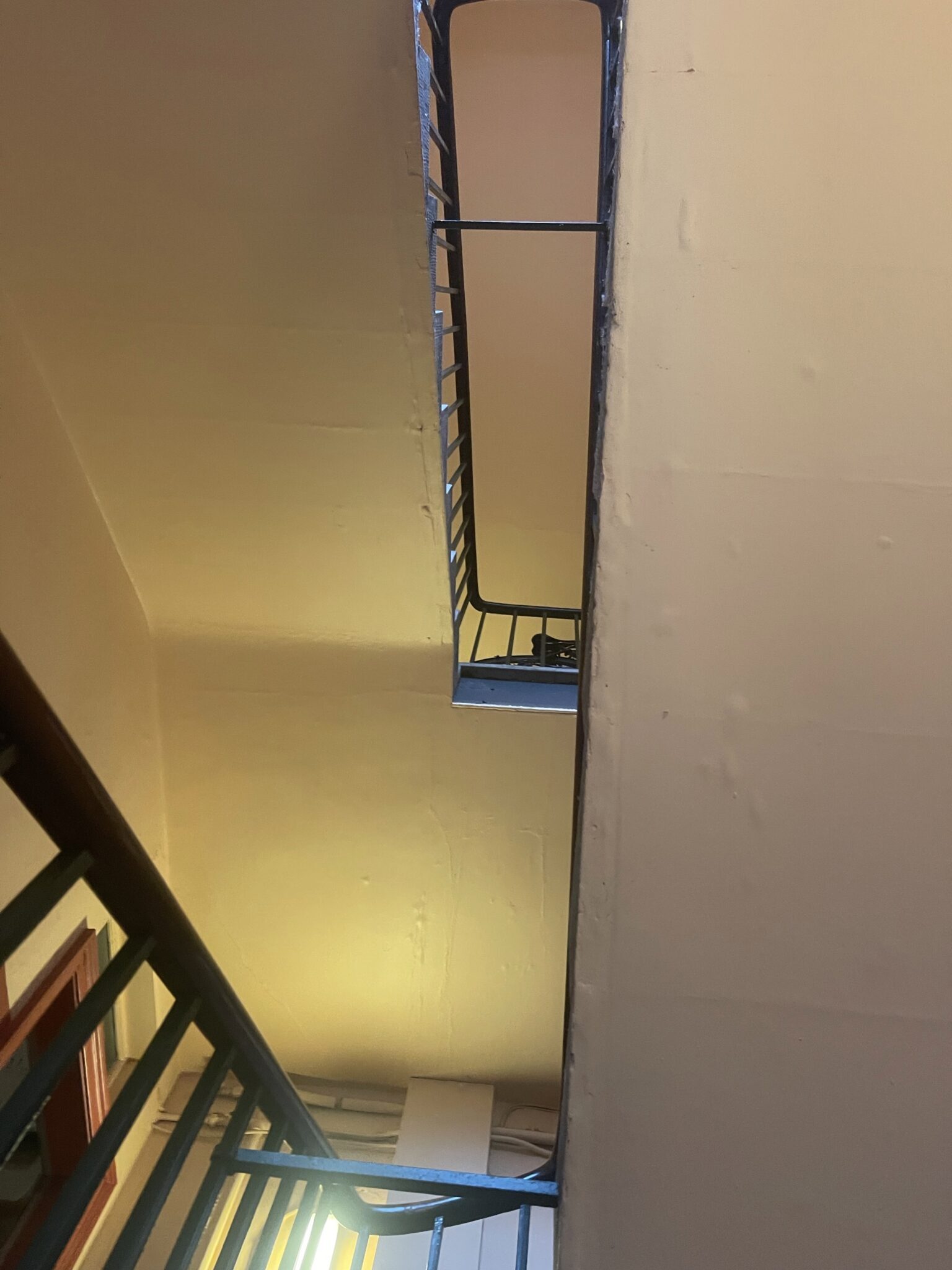 Looking up a tall communal stairwell with black railings inside a period building in Hove