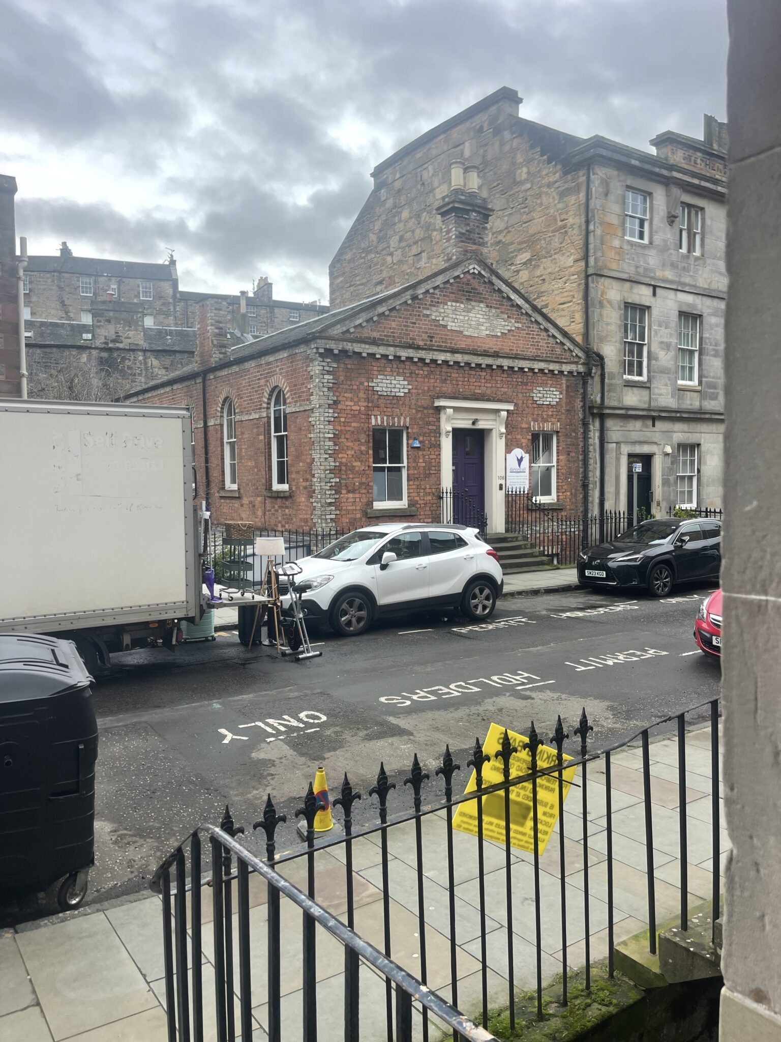 ESV Removals Luton van parked on an Edinburgh street of sandstone tenements, furniture staged on the pavement and PERMIT HOLDERS ONLY painted on the road