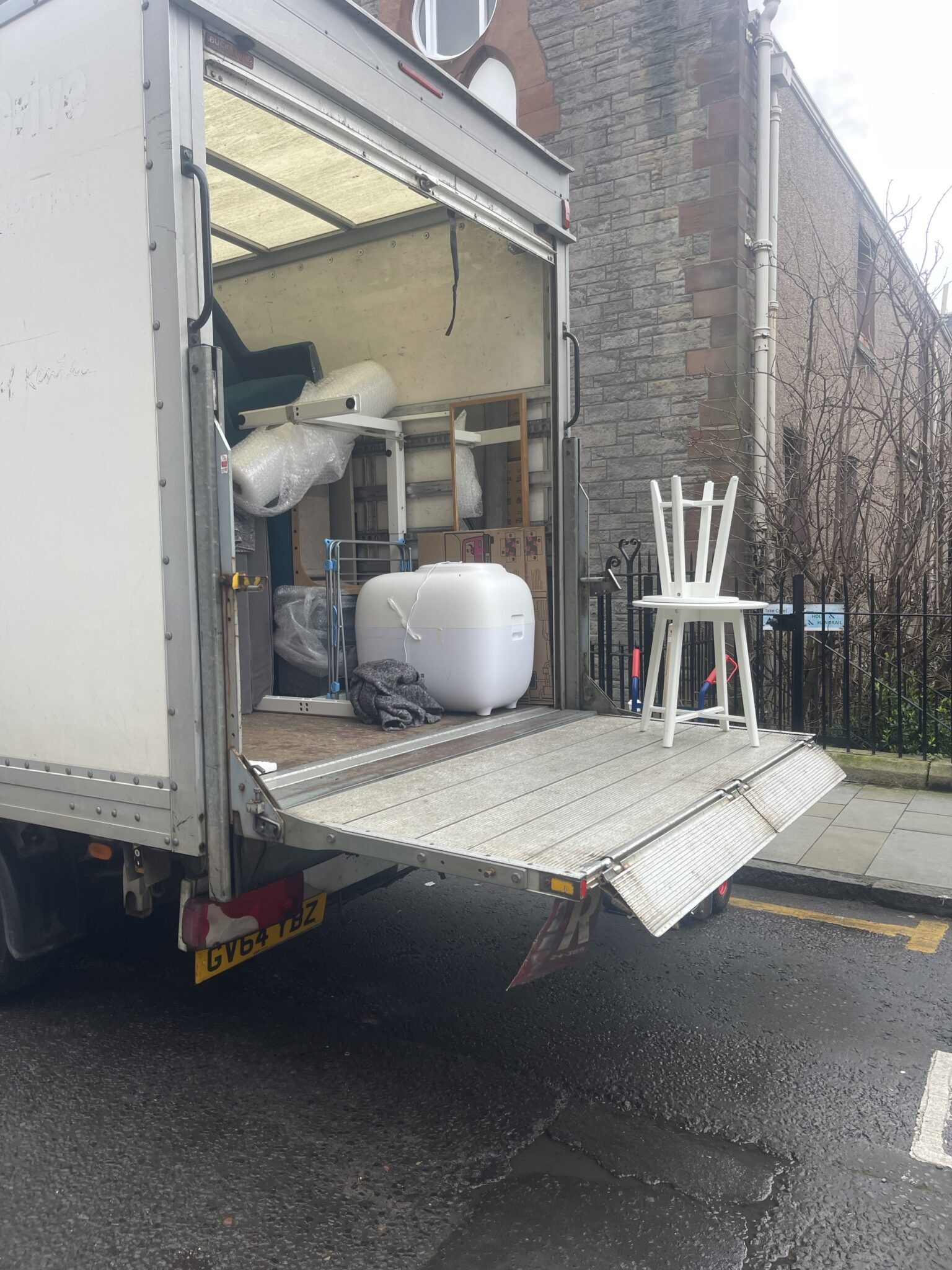 ESV Removals Luton van with its tail lift down on an Edinburgh street, with a white chair and household items waiting to be carried in