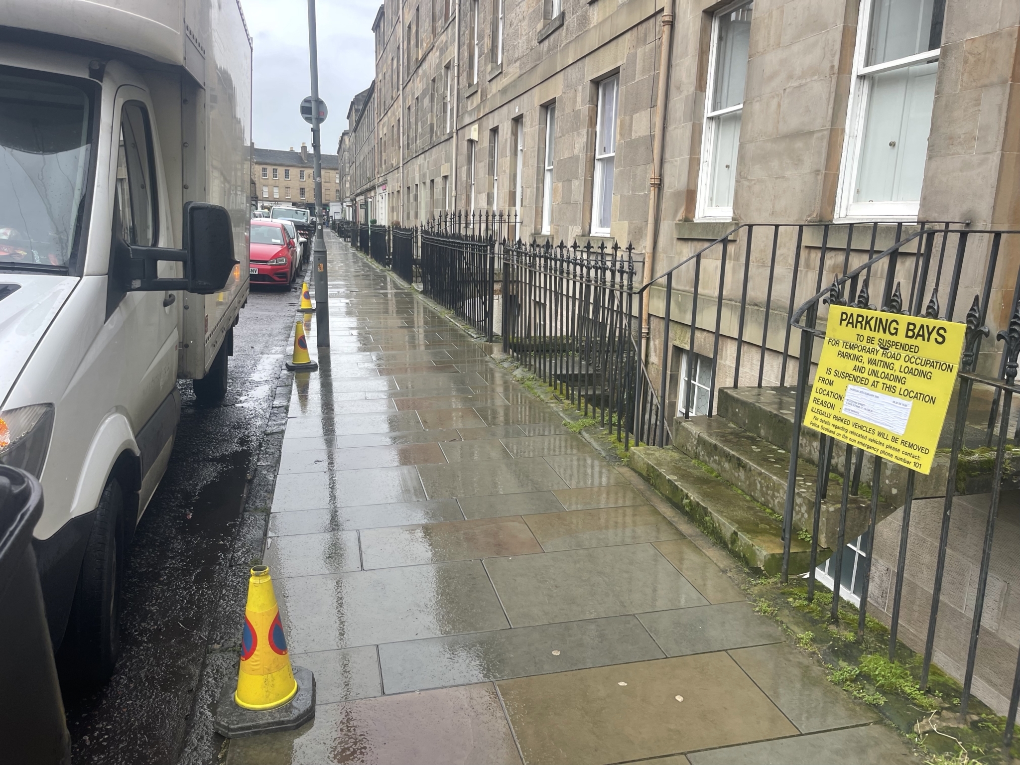 Luton van parked beside cone marked suspended parking bays on a wet Edinburgh tenement street, showing the planned legal stopping point for unloading.