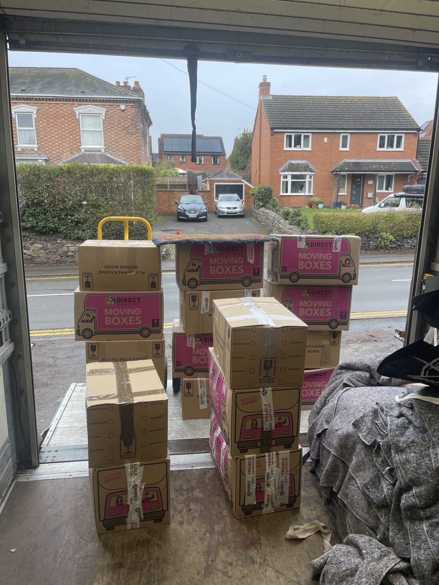 Stacked moving boxes staged at the tail lift of an ESV Removals Luton van, ready for a tidy unload on a residential street in Loughborough.