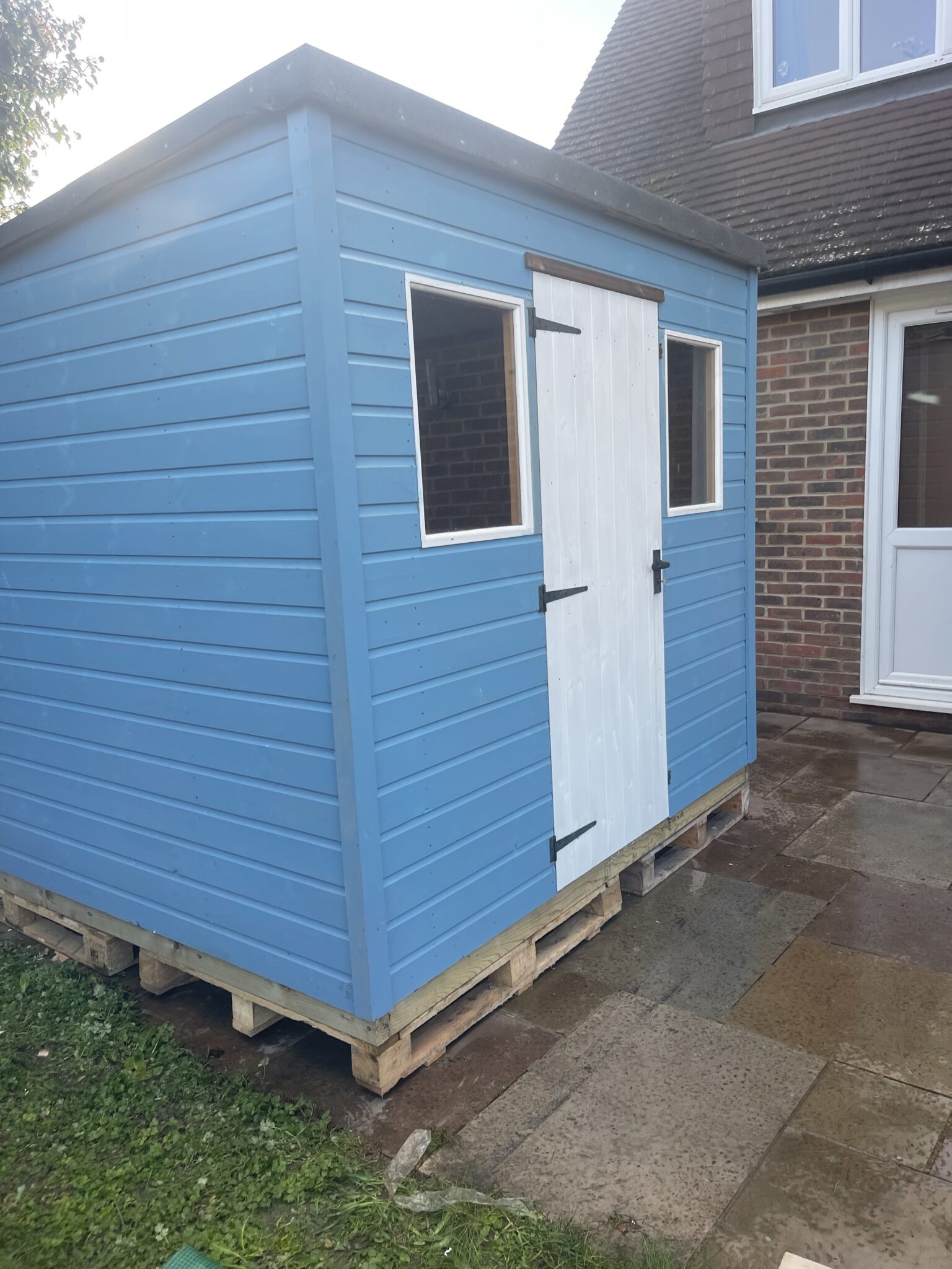 Reassembled blue shed on new raised base with aligned door and windows at Worthing property