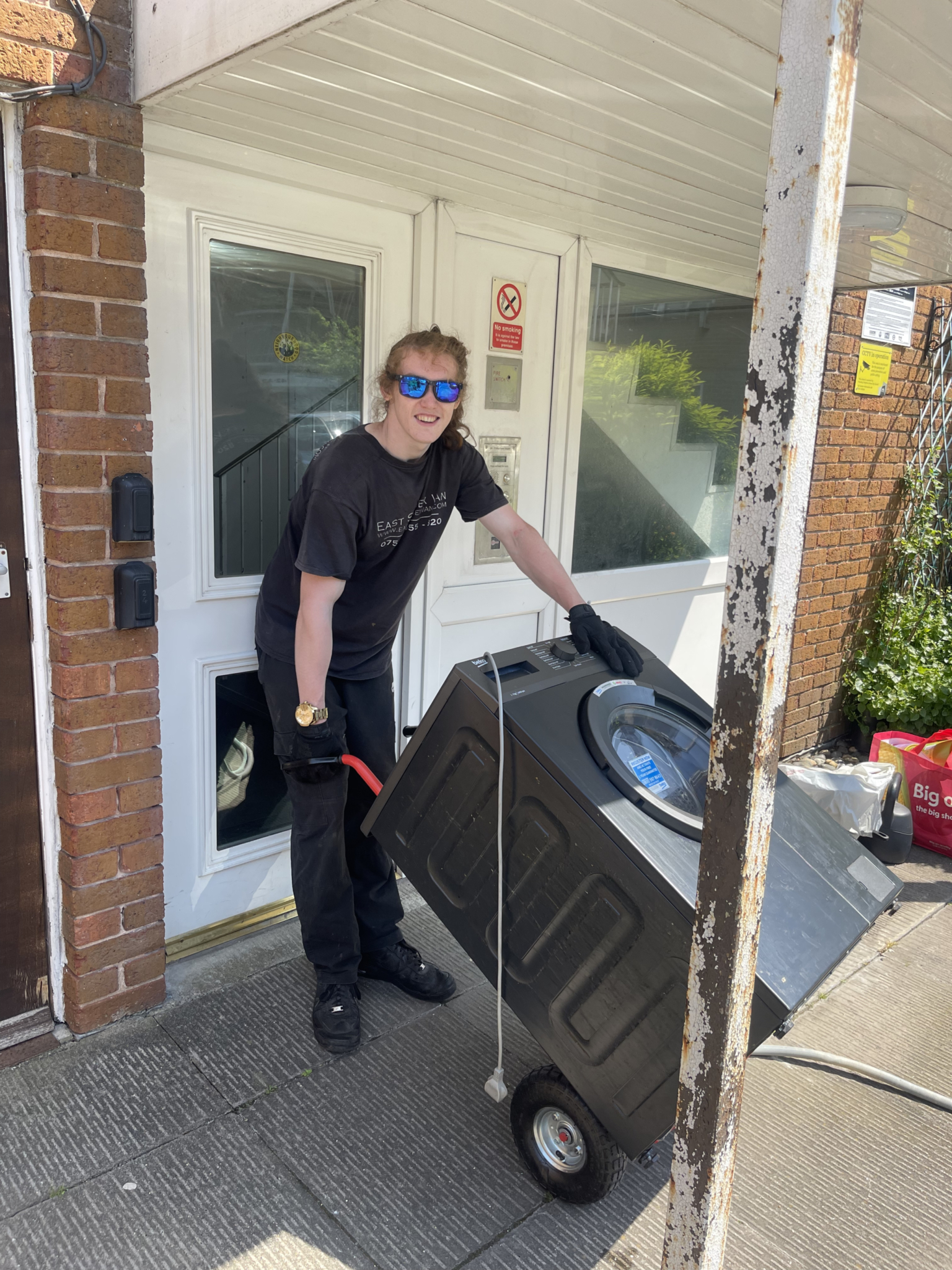 Worthing removals crew member using an appliance trolley to move a washing machine outside a residential entrance.