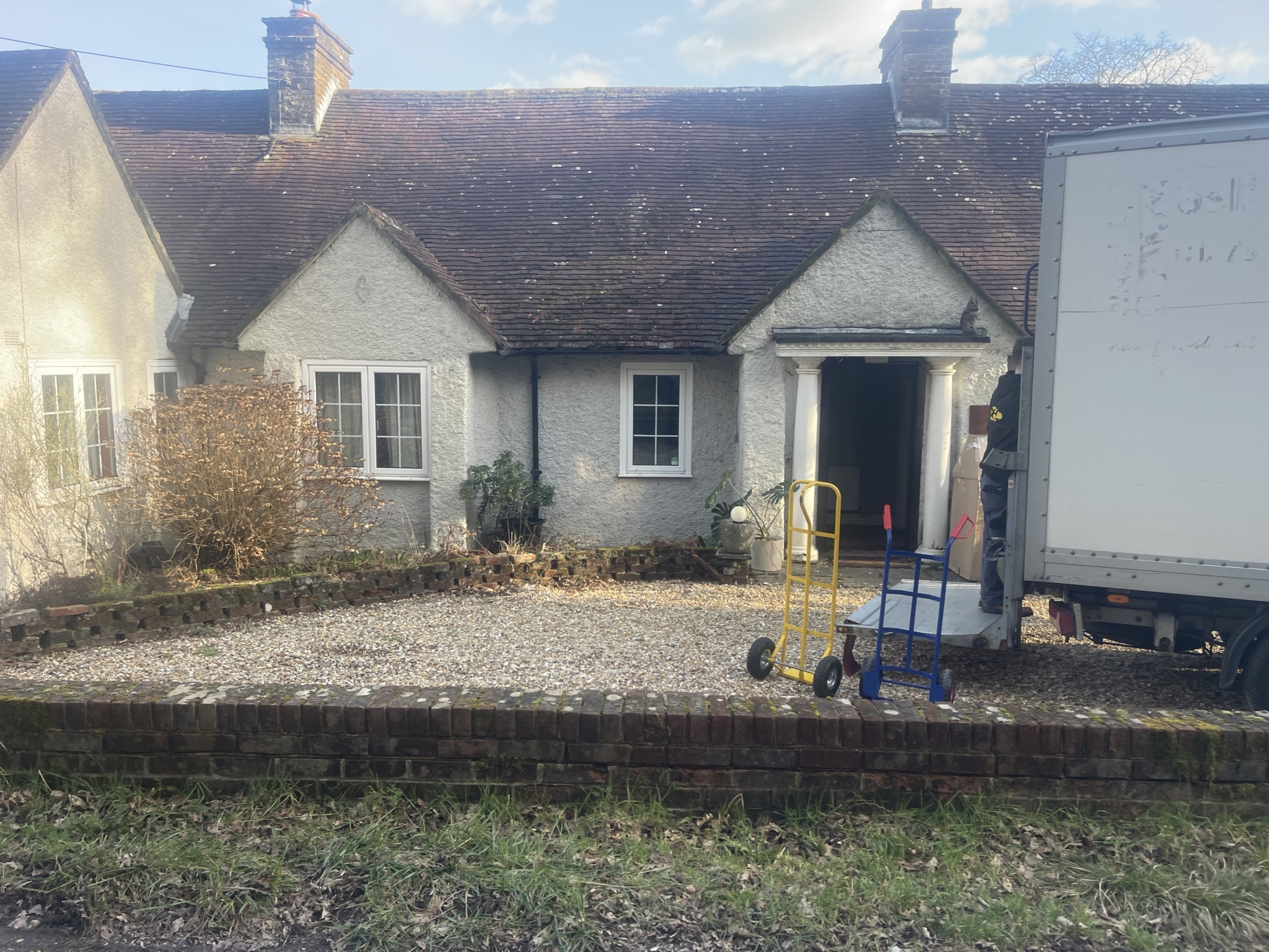 ESV Removals Luton van unloading at a traditional Wivelsfield bungalow, with sack trolleys ready at the driveway and the front door open for delivery.