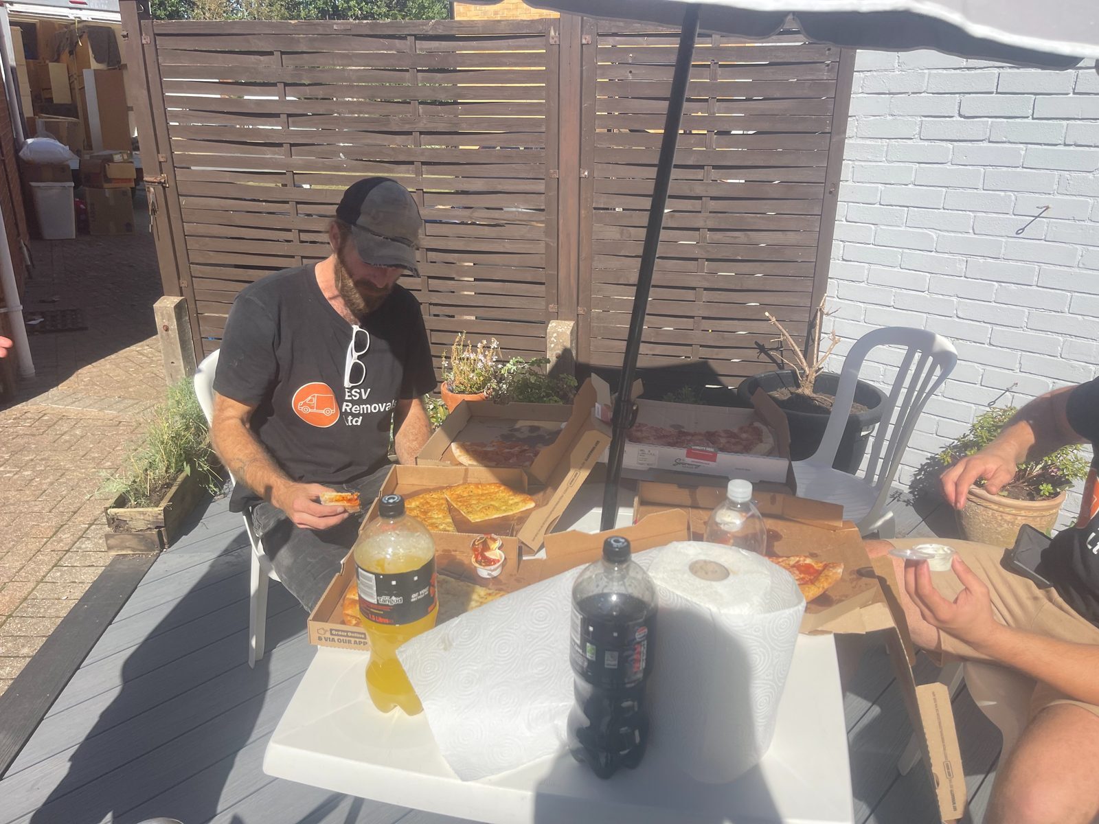 ESV Removals crew member in a branded t-shirt sitting down to a pizza lunch at an outdoor table during a moving day break