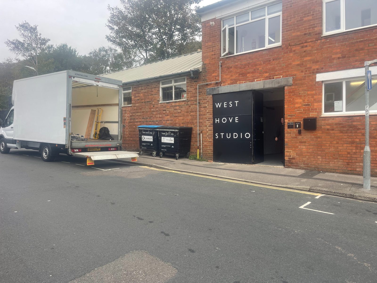 ESV Removals Luton van with its tail lift down parked outside a red brick studio building in West Hove