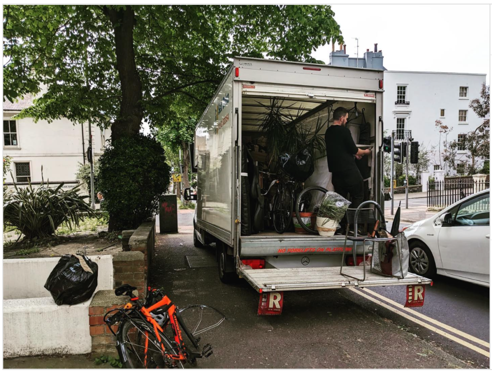 Luton removals van parked on a residential street in Seven Dials, Brighton, with the tail lift down and a mover inside the van among bikes, plants, and household items.