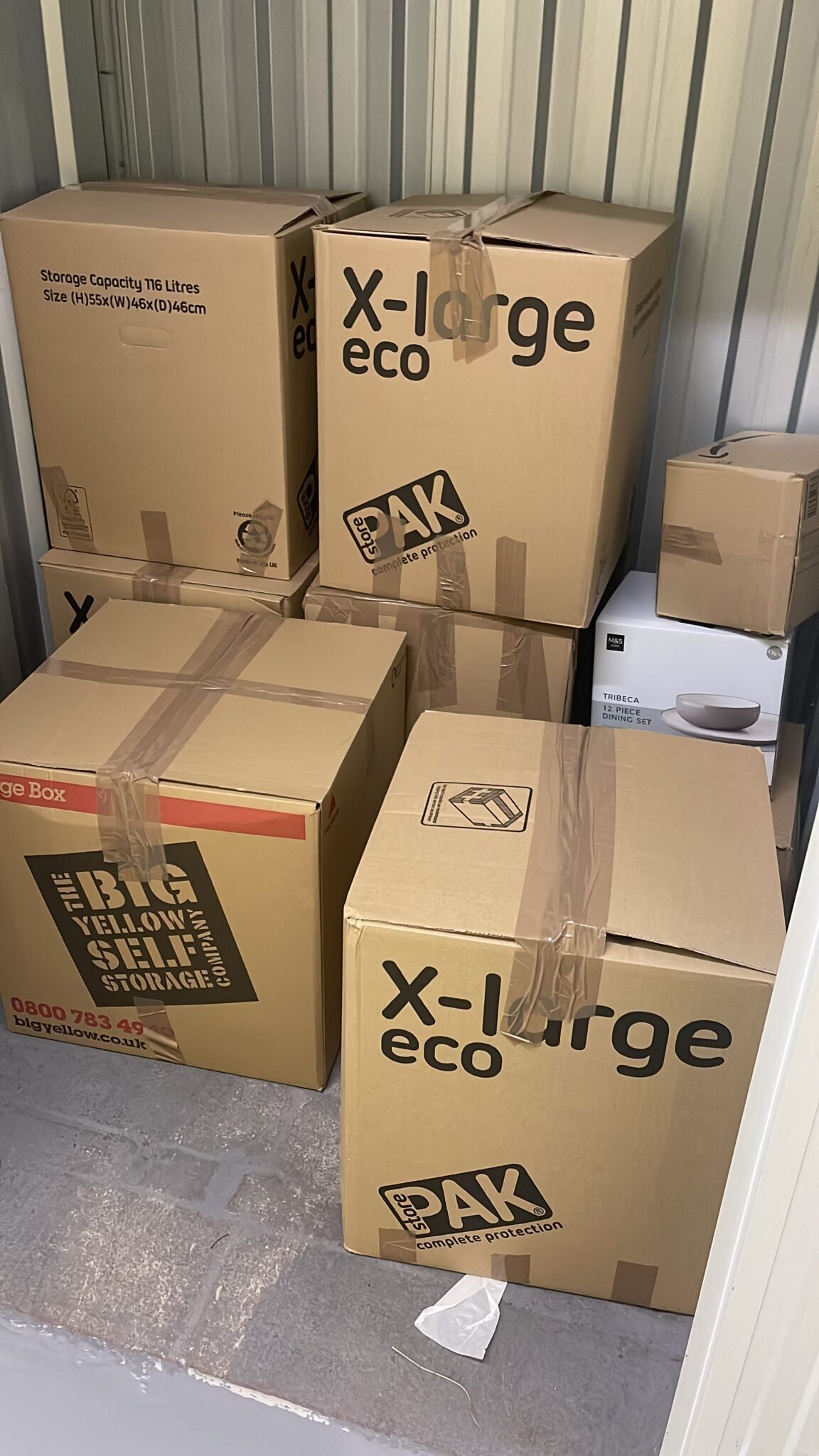 Stacked moving boxes neatly arranged inside a storage unit, including extra large eco boxes and a boxed dining set ready for short or long term storage.