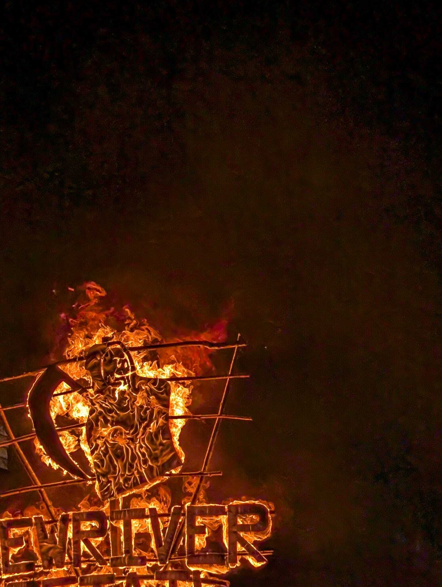 A burning bonfire tableau at night, a flaming metal frame spelling out NewRiver beneath a figure