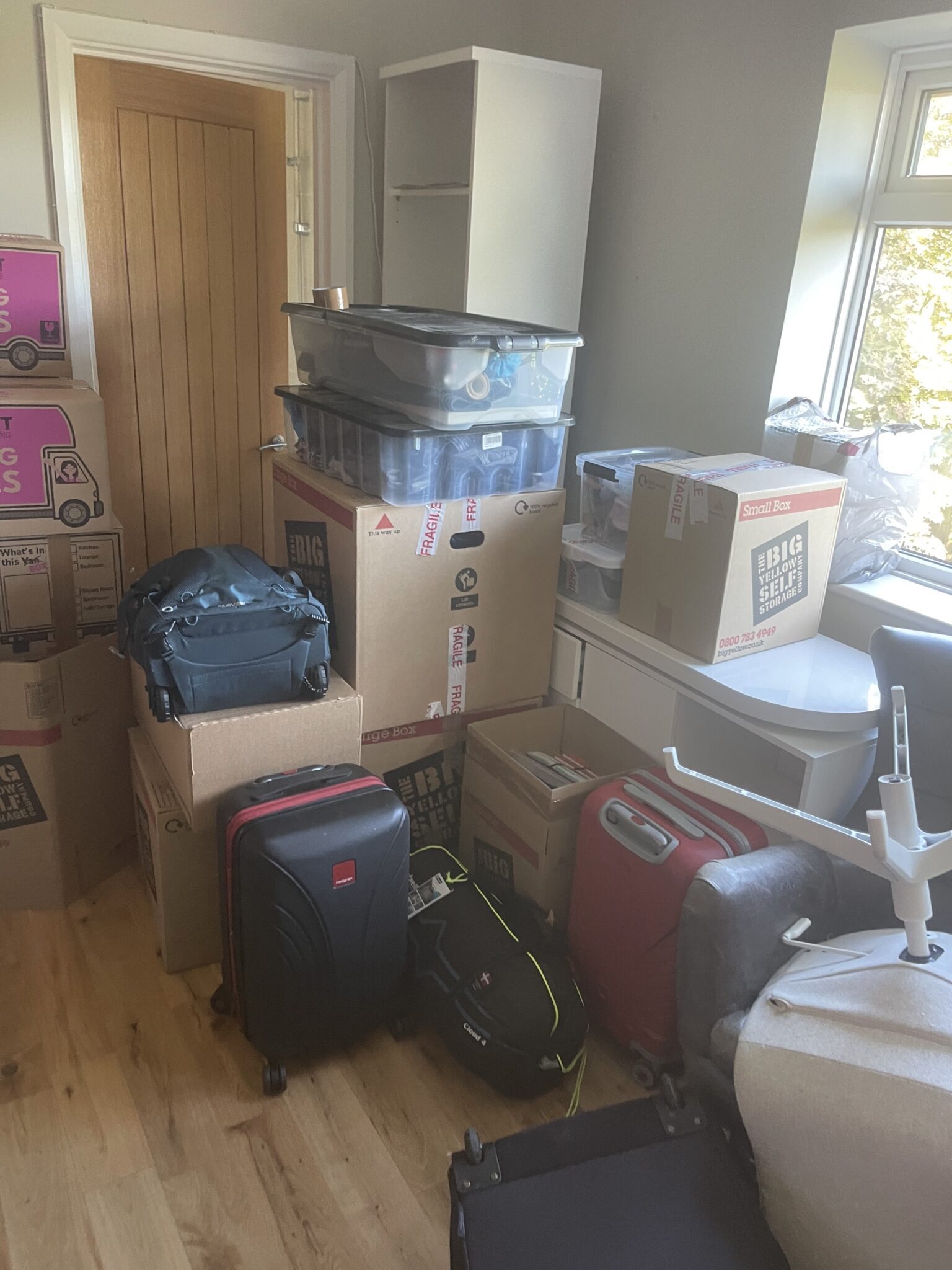 Packed moving boxes labelled with fragile tape and this-way-up markings, including Big Yellow Self Storage boxes, staged in a bedroom with suitcases ahead of an ESV Removals collection.